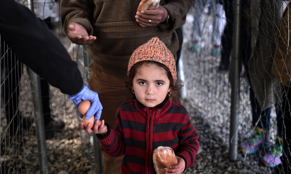 Una niña migrante recibe un sándwich en el campamento improvisado en la frontera entre Grecia y Macedonia, cerca del pueblo griego de Idomeni, el 2 de marzo de 2016, donde se encuentran miles de personas.AFP/LOUISA GOULIAMAKI
