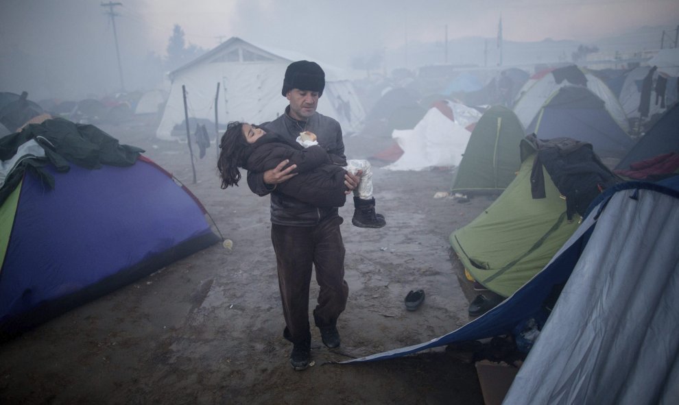 Un hombre lleva su hija en brazos sobre el barro tras las fuertes lluvias caidas durante la noche en una fría mañana en el campo de refugiados .- EFE