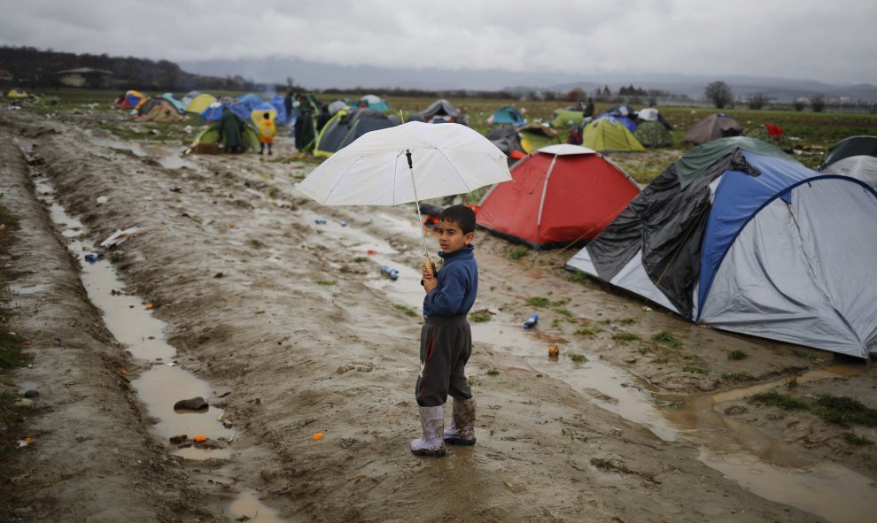 Un niño migrante del campamento improvisado en la frontera entre Grecia y Macedonia sujeta su paraguas, Grecia. REUTERS / Stoyan Nenov