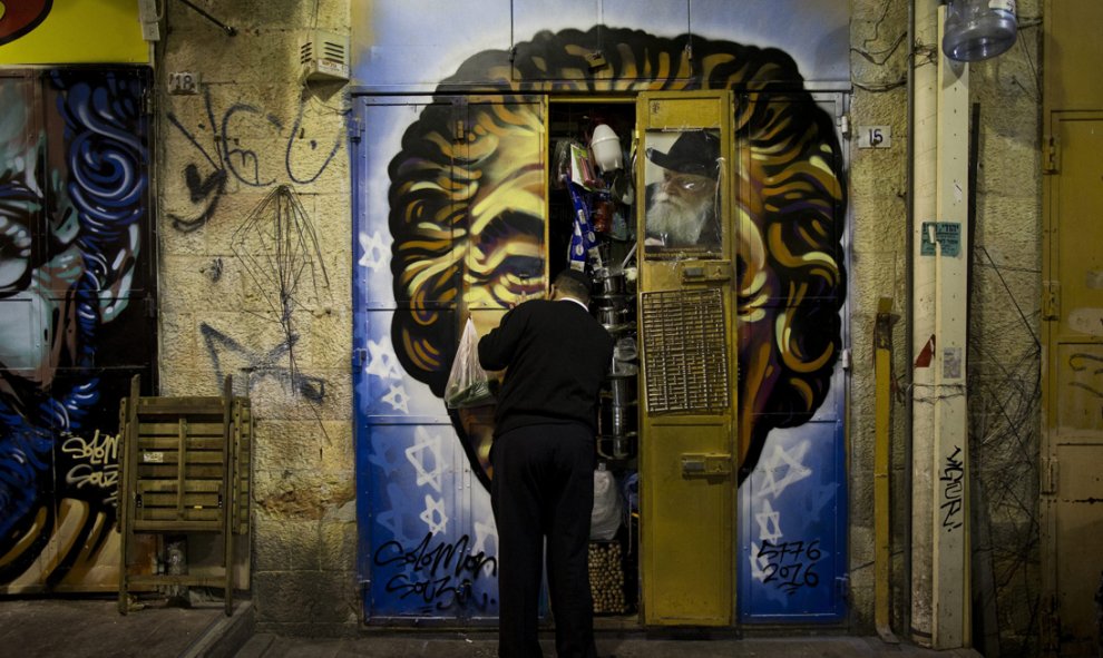 Un comerciante cierra las puertas de su establecimiento en el mercado Mahane Yehuda, decorado con un grafiti del artista callejero Solomon Souza, en Jerusalén. EFE/Abir Sultan