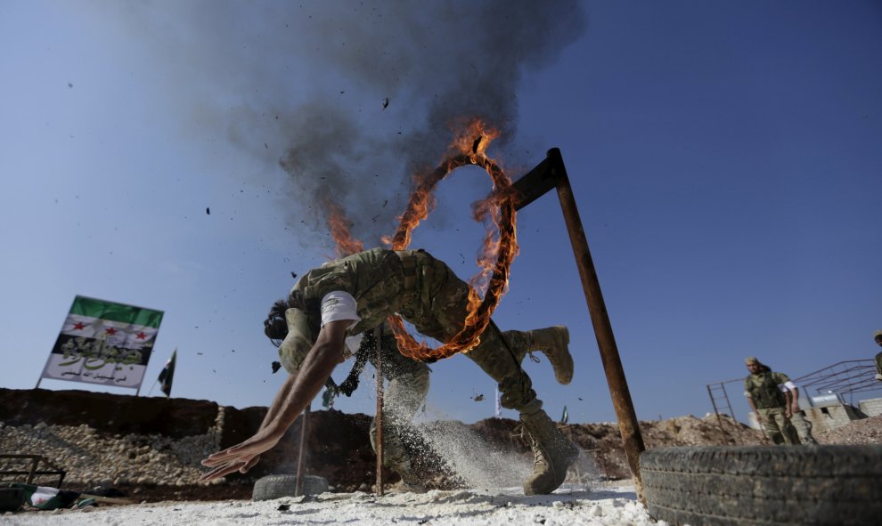 Un combatiente rebelde salta a través de un circuito de fuego como demuestra su habilidad durante una exhibición militar como parte de una ceremonia de graduación en un campamento en el norte de la provincia de Hama, Siria 31 de marzo de 2016. REUTERS / K