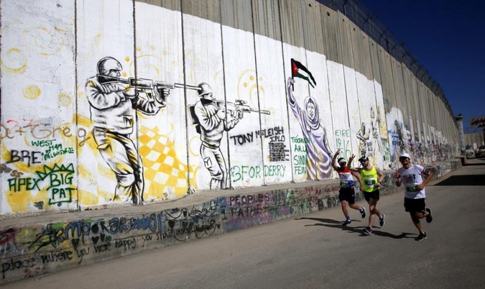 Participantes compiten junto al muro de separación durante la Maratón 'Derecho al Movimiento' en la ciudad cisjordana de Belén. Unas 4.300 personas han recorrido las calles de esta ciudad palestina durante la celebración de la cuarta carrera anual que def