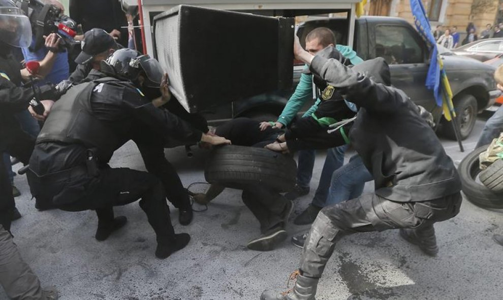 Agentes de policía intentan quitar un neumático de las manos de un manifestante, durante una protesta celebrada frente al despacho presidencial en Kiev, Ucrania. EFE/Sergey Dolzhenko