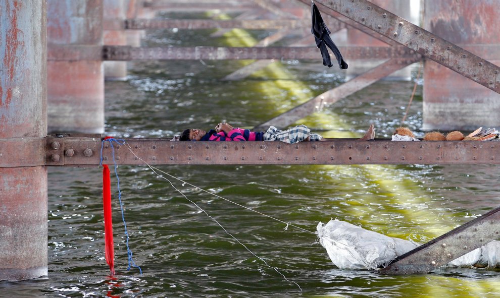 Un hombre duerme en una viga entre los dos pilares de un puente sobre el río Sabarmati durante un día caluroso en Ahmedabad, India. REUTERS/Amit Dave