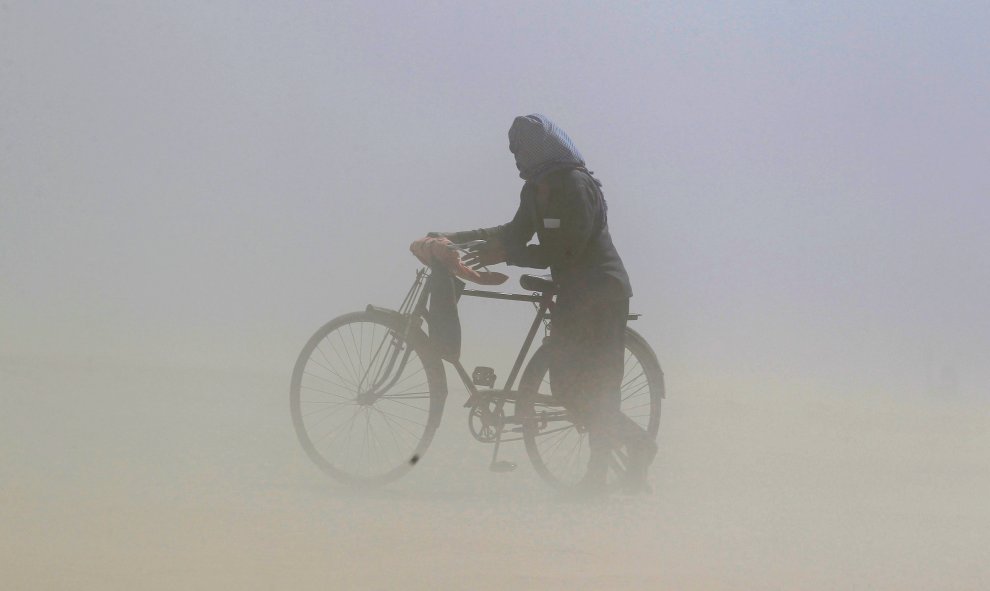 Un hombre cubre su rostro mientras empuja una bicicleta durante una tormenta de arena junto al río Ganga, en Allahabad, India. /REUTERS-Jitendra Prakash