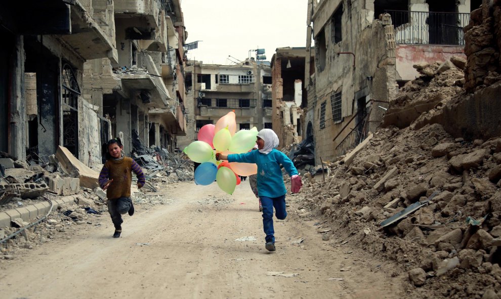 Niños sirios juegan con globos entre edificios dañados en el barrio de Jobar, a las afueras de la capital siria de Damasco. AMER ALMOHIBANY / AFP