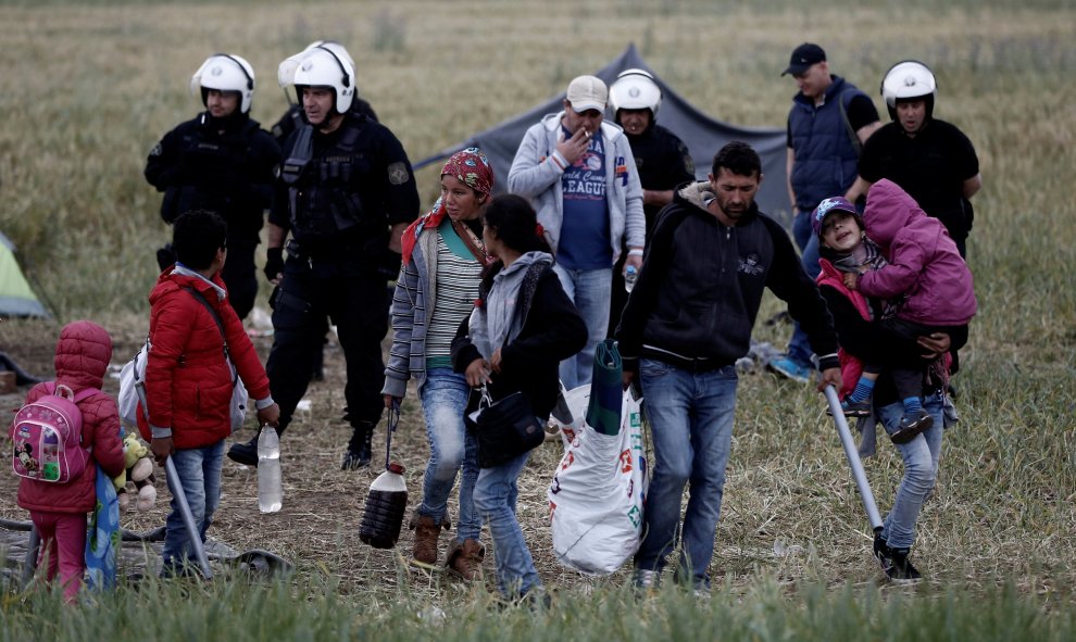 Una familia de refuigiados recoge sus pertenecias ante la mirada de agentes de la policía durante el desajolo del campamento de Idomeni, en la frontera entre Grecia y Macedonia. REUTERS/Yannis Kolesidis