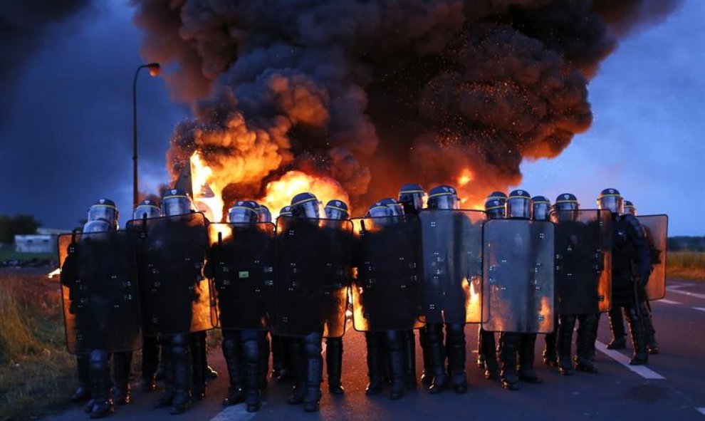 Agentes antidisturbios franceses avanzan delante de una barricada en llamas para proceder al desalojo de los manifestantes que bloquean la entrada a una refinería en Douchy-les-Mines, al noreste de Francia. EFE/Thibault Vandermersch