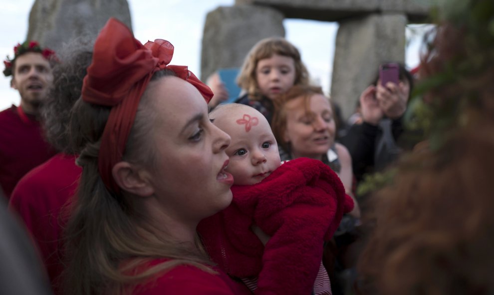 Una mujer lleva a su bebé a celebrar el solsticio de verano en Stonehenge, vestidos de rojo