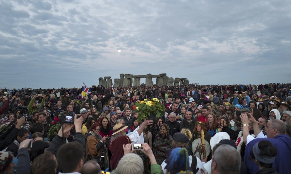 Un visitante ofrece flores ante la multitud durante el anochecer en Stonehenge