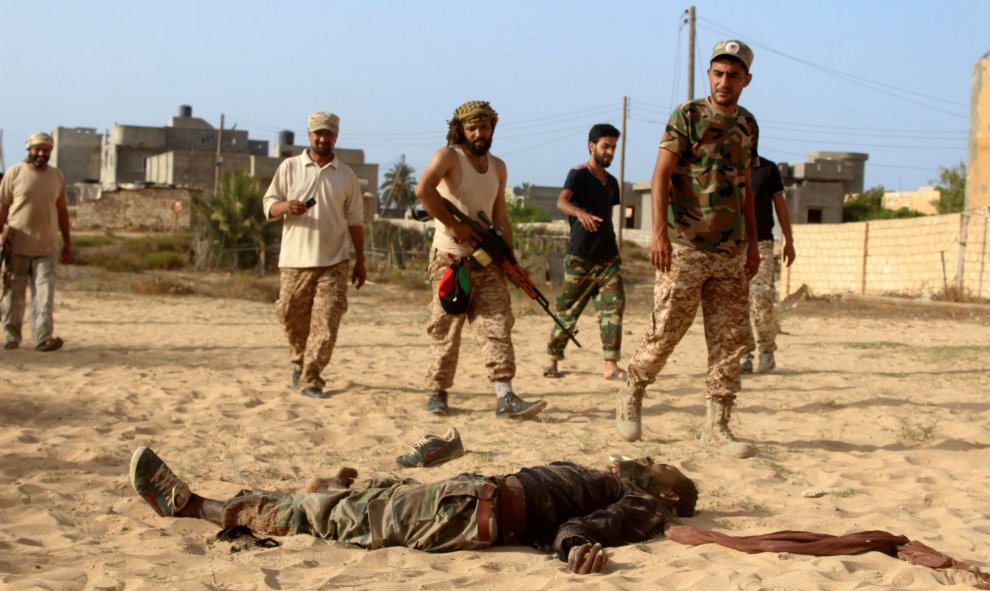 Combatientes de las fuerzas afines al nuevo gobierno de unidad de Libia pasan junto al cadáver de un luchador del Estado Islámico en la zona de Zaafran en Sirte.- REUTERS