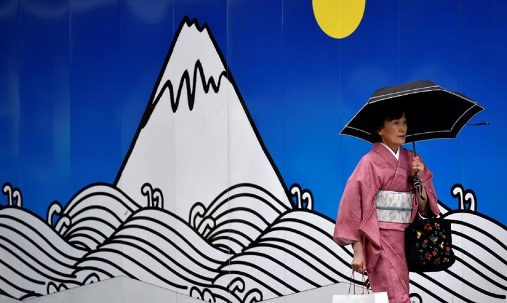 Una mujer vestida con un kimono pasa delante de un andamio decorado con el dibujo de una montaña en el distrito comercial de Ginza en Tokio, Japón. EFE/Franck Robichon