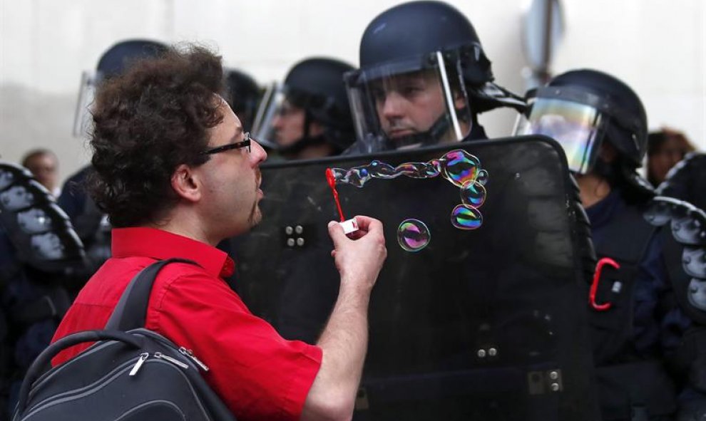 Un manifestante hace pompas de jabón ante efectivos de la policía antidisturbios, durante una protesta convocada contra la reforma laboral del Gobierno socialista en París, Francia. EFE/Ian Langsdon