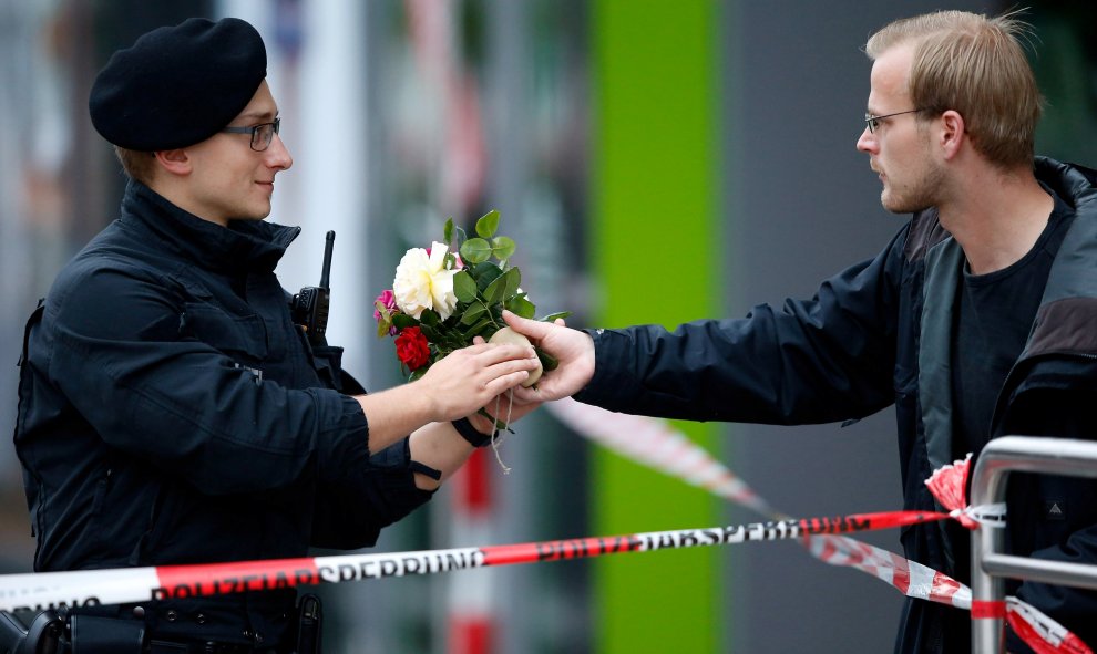 Un hombre entrega un ramo de flores a uno de los policías que custodian el lugar del tiroteo. - REUTERS