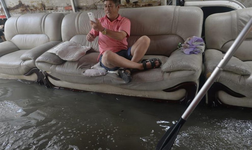 Fotografía que muestra a un hombre sentado en un sofá mientras toma fotos de las inundaciones, en Shenyang, provincia de Liaoning, al nordeste de China. EFE/Stringer