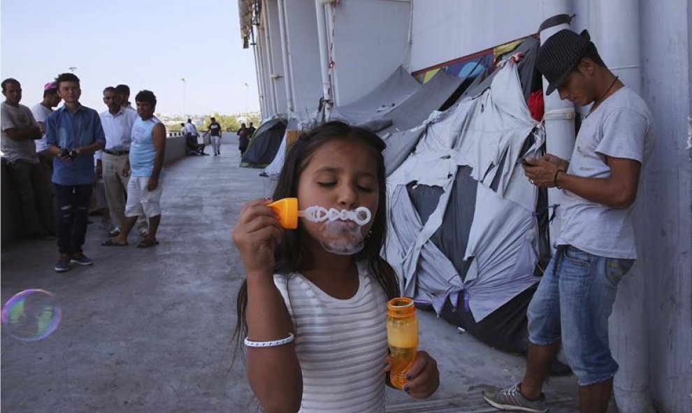 Una niña afgana juega con pompas de jabón en el campamento de refugiados de Hellinikon, en Atenas (Grecia). Unos 57.000 refugiados están acogidos en alguno de los campamentos distribuidos por el país. EFE/Orestis Panagiotou