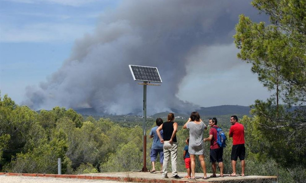 Unos vecinos observan el incendio en La Pobla de Montornès (Tarragona) donde los Bomberos han desalojado hoy la parte alta de la urbanización Castell de Montornès como medida de precaución ante un incendio que arde sin control en una zona forestal de difí