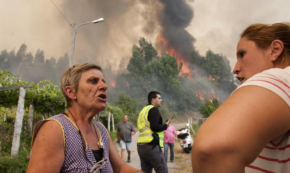 Dos vecinas hablan ante las llamas, que cada vez se acercan más a la población de Arbo (Pontevedra), donde se ha decretado "Situación 2"/EFE