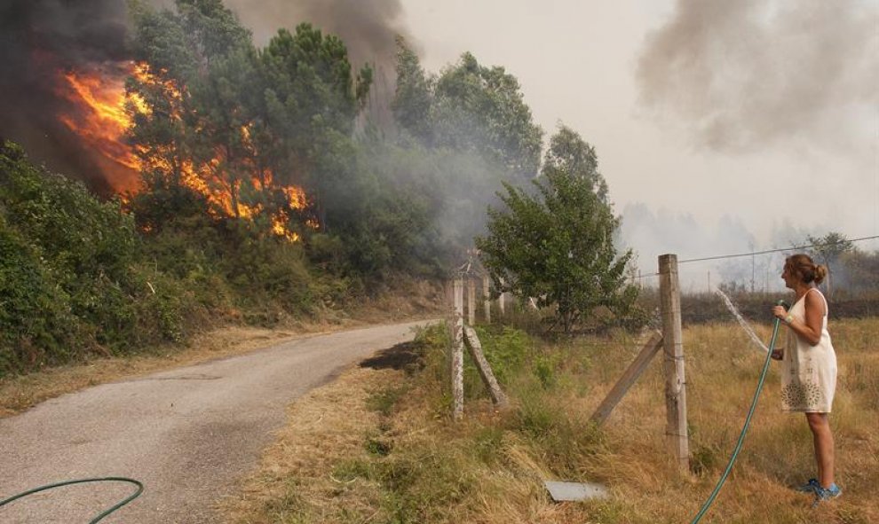 Una mujer observa como se acerca el fuego en Pontevedra con una manguera en la mano/EFE