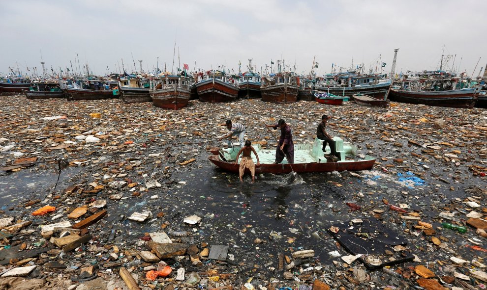 Niños a bordo de un barco abandonado recoge los objetos reciclables a través de aguas contaminadas en frente de barcos de pesca en el puerto de pescado en Karachi , Pakistán. REUTERS / Akhtar Soomro