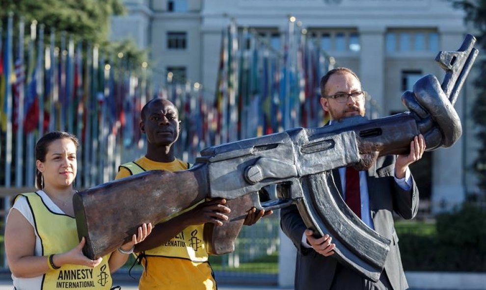 Activistas de Amnistía Internacional sujetan una réplica de un fusil AK-47 con el cañón torcido durante una protesta contra el Tratado sobre Comercio de Armas (ATT) en la segunda conferencia de estados miembros de este tratado (CSP2), delante de la sede e