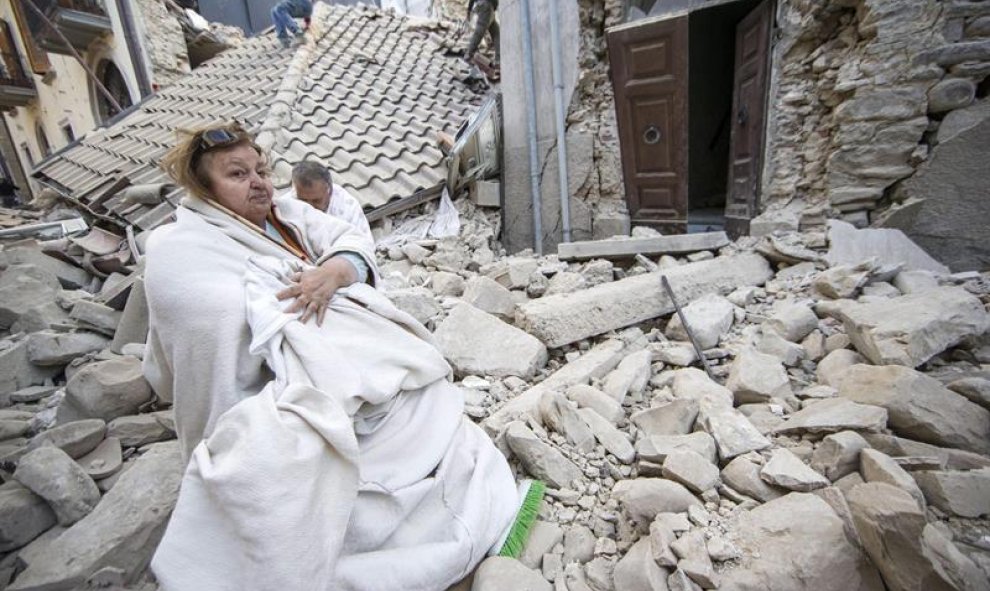 Una mujer permanece sentada sobre los restos de lo que era su casa tras ser derruida a causa del terremoto en Amatrice/EFE