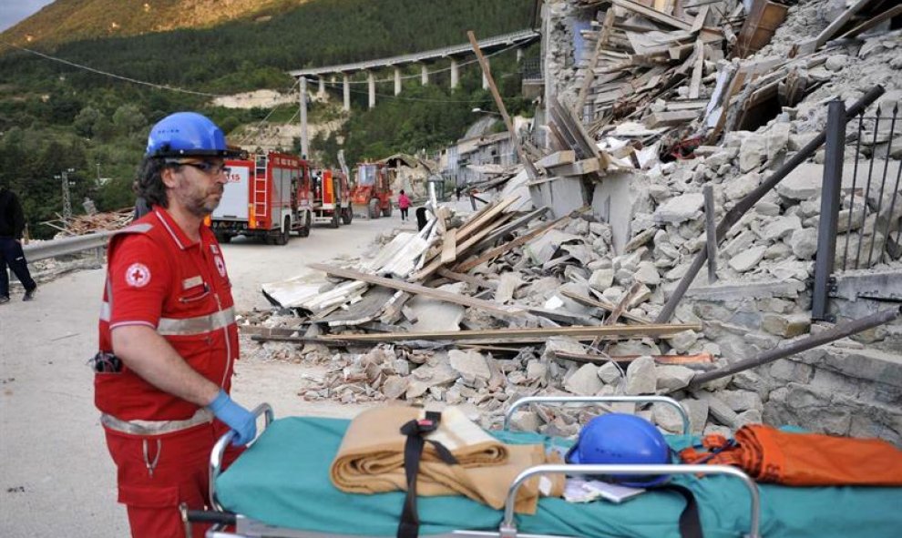 Un trabajador de la Cruz Roja italiana espera con una camilla a uno de los rescatados de entre los escombros en un edificio en Pescara del Tronto/EFE