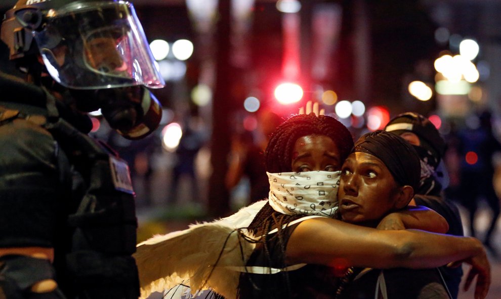 Dos mujeres se abrazan con la mirada asustada junto a un policía en Charlotte, Carolina del Norte durante la protesta. REUTERS / Jason Miczek