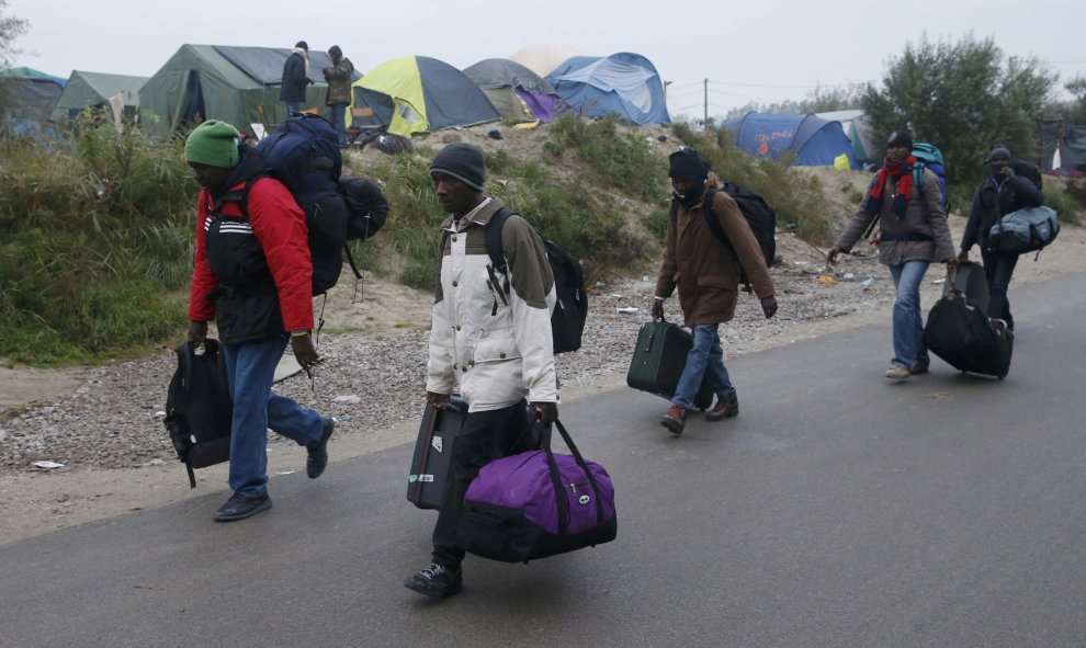 Un grupo de refugiados caminan con sus pertenencias junto a las tiendas de campaña de la 'Jungla' de Calais  durante el desmantelamiento de esta. REUTERS/Pascal Rossignol