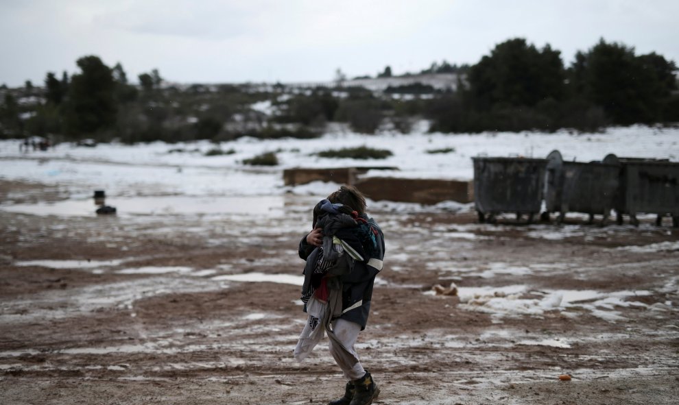 Una niña carga con ropa en el nevado campo de refugiados de Ritsona, en el norte de Atenas. REUTERS/Alkis Konstantinidis