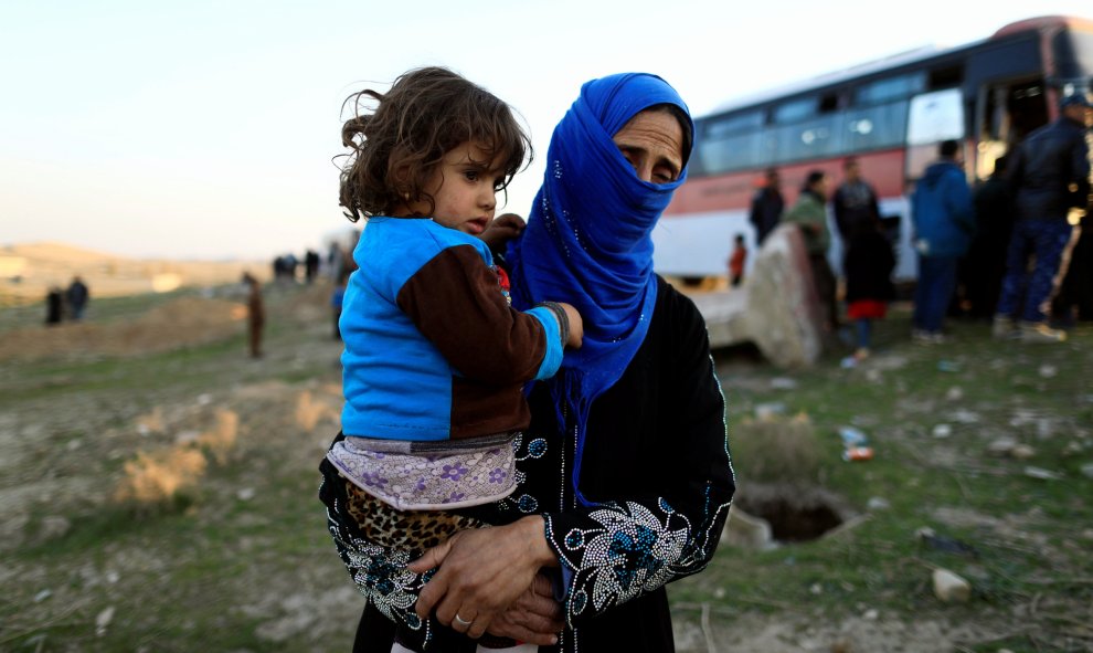 Una mujer, que acaba de huir de una aldea controlada por los militantes del Estado islámico, sostiene a su hija mientras se encuentra frente a un autobús antes de dirigirse al campamento de Hammam Ali, al sur de Mosul, Irak. REUTERS/Zohra Bensemra