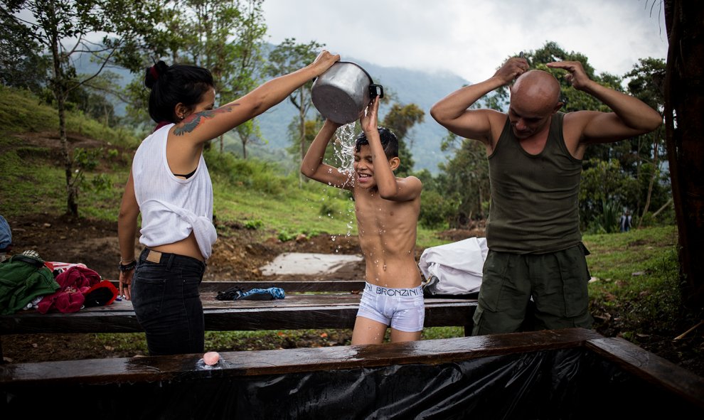 Una pareja de guerrilleros aseándose, junto al hijo de uno de ellos, en el campamento de desmovilizados de las FARC en La Fila, Tolima. El Gobierno no ha construido las infraestructuras básicas de habitabilidad que prometió en los acuerdo de paz.- JAIRO V