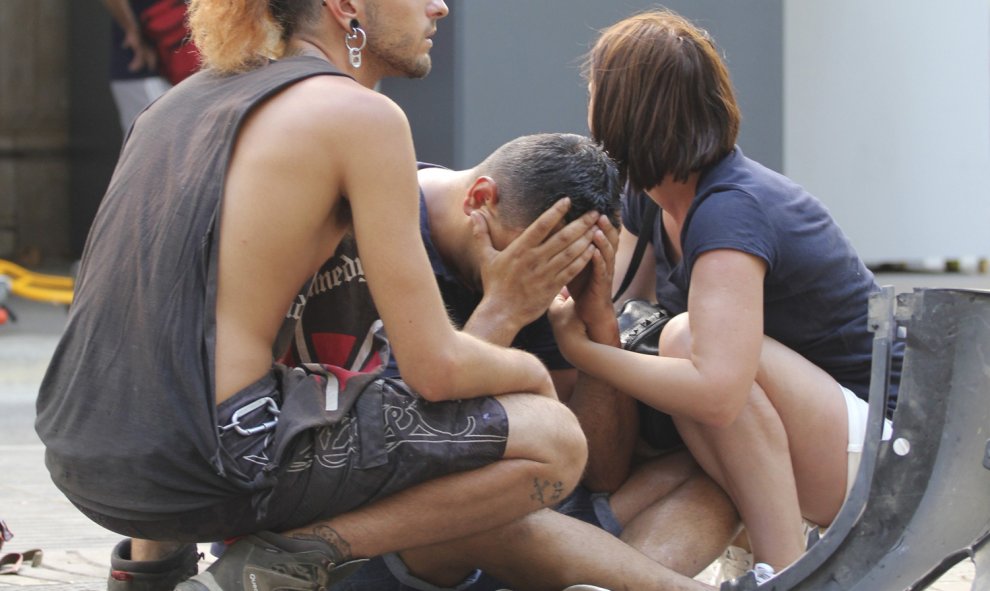 Varios jóvenes permanecen junto a los restos de un vehículo, en el lugar del atropello masivo de una furgoneta que ha arrollado esta tarde a varias personas que paseaban por las Ramblas de Barcelona.- EFE