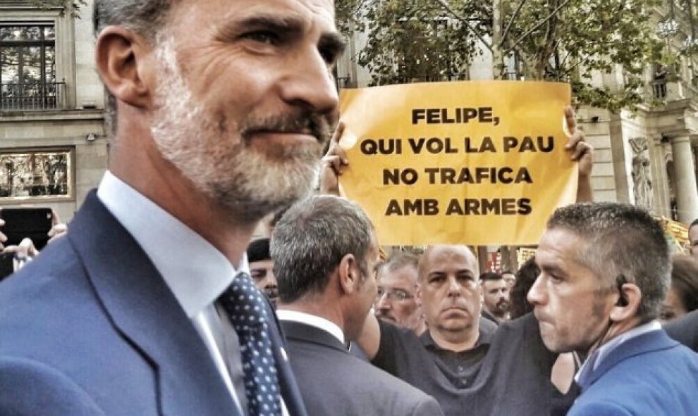 Imagen recogida de Twitter en la que Felipe VI pasa justo por delante de un de un manifestante que sujeta una pancarta con el lema: "Quien hace la paz no trafica con armas".