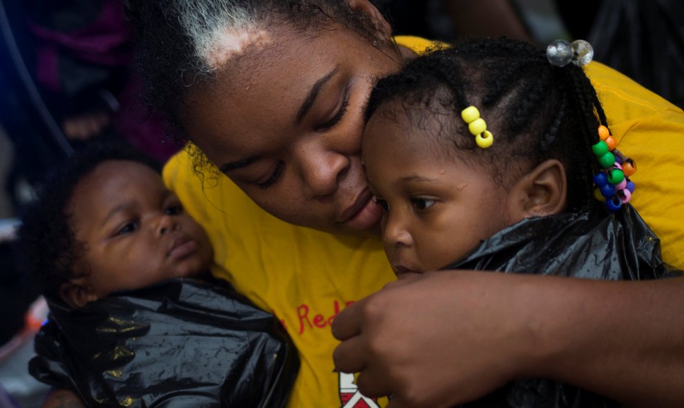 Laquanta Edwards sostiene a su hija de un año Ladaja (D) y a su hijo LaDarius, de nueve meses, después de ser evacuados a tierras altas en barco debido a las inundaciones causadas por la tormenta tropical Harvey a lo largo de Tidwell Road en Houston este,