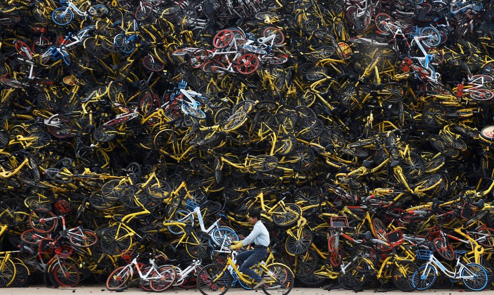 Un trabajador  conduce una bicicleta compartida junto una enorme pila de bicicletas compartidas sin usar en un terreno baldío en Xiamen, provincia de Fujian, China. La infraestructura y las regulaciones chinas no estaban preparadas para una inundación rep