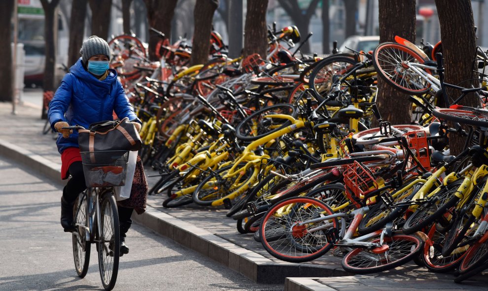 Una mujer pasa junto a varias bicicletas compartidas tiradas en el suelo en una carretera en Pekín. China ha emitido pautas nacionales que rigen las operaciones de bicicletas compartidas en 2017 en un esfuerzo por nutrir una nueva industria acreditada com