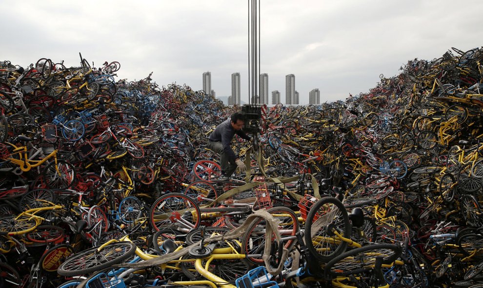 Un trabajador desenreda una cuerda en medio de miles de bicicletas apiladas en un lote en Xiamen, provincia de Fujian, China. A medida que algunas de las empresas crecieron demasiado en muy poco tiempo fueron quebrando y se retiraron, por lo que sus bicic