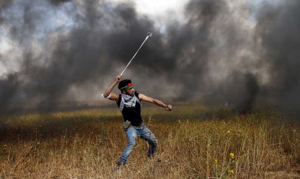 Un joven palestino arroja piedras a las tropas israelíes durante los enfrentamientos en una jornada protestas en las que ha colocado tiendas de campaña a lo largo de la frontera de Israel con Gaza, exigiendo el derecho a regresar a su tierra natal.- REUTE