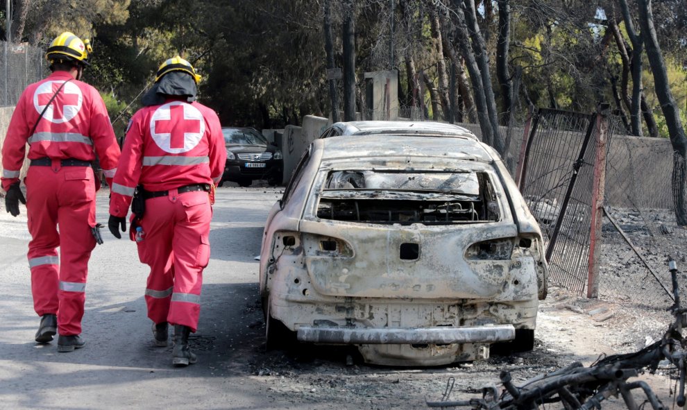 Miembros de la Cruz Roja caminan junto a un vehículo calcinado en una zona afectada por los incendios en Argyra Akti, en Mati (Grecia).  EFE/Pantelis Saitas