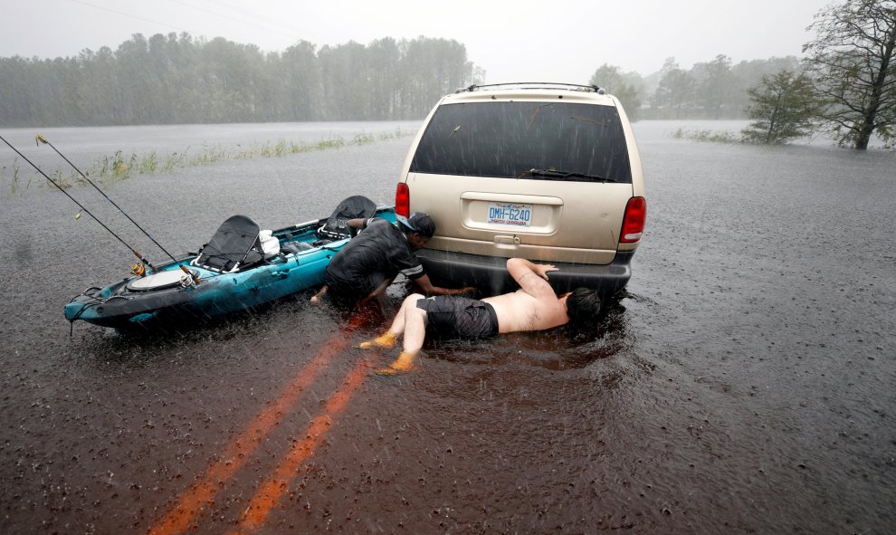 Dos hombres intentan arreglar un coche que está en medio de la carretera y al que han llegado en canoa | REUTERS/Jonathan Drake