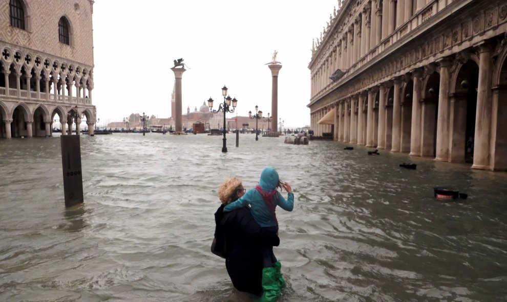 Una mujer sostiene a una niña mientras camina en una inundada plaza de San Marcos. Reuters / Manuel Silvestri