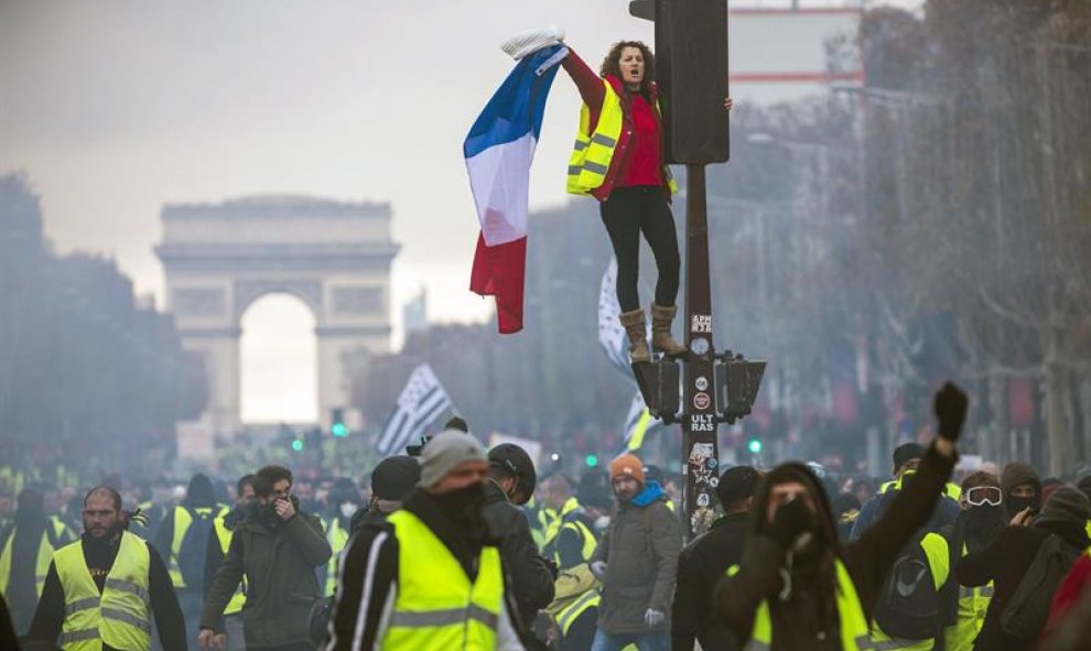 Una mujer grita consignas subida a un semáforo durante una protesta en los Campos Elíseos en París (Francia) hoy, 24 de noviembre de 2018. El ministro francés del Interior, Christophe Castaner, culpó hoy a la ultraderecha y a su líder, Marine Le Pen, de l