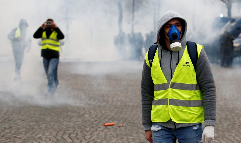 Varios manifestantes de los chalecos amarillos ocultan su rostro con mascaras de humo para evitar respirar los gases lacrimógenos lanzados por la Policía en París. REUTERS/Stephane Mahe