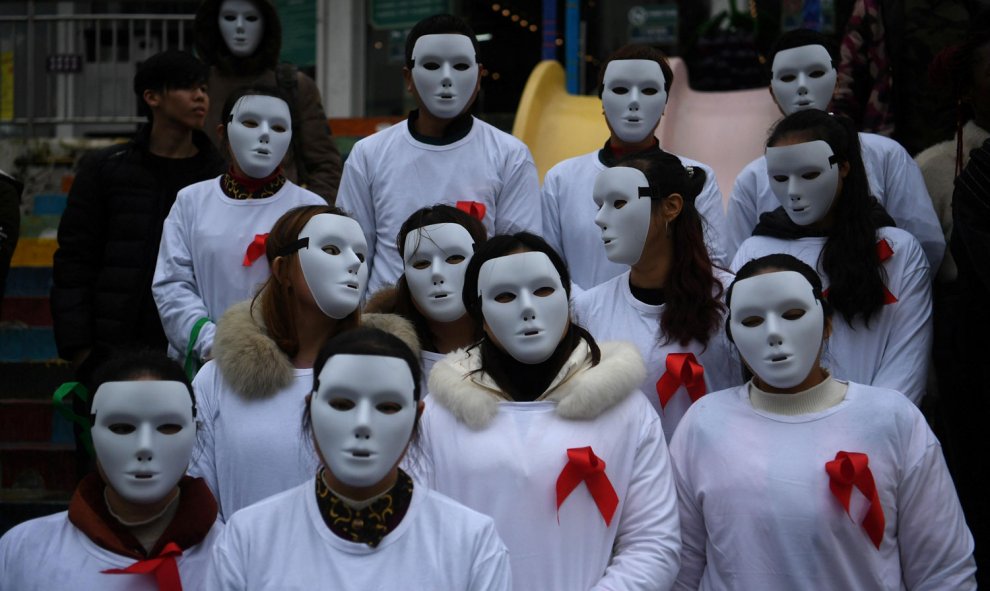Voluntarios con máscaras blancas y cintas rojas en sus camisetas participan en un evento para crear conciencia sobre el Sida en Chongqing.- REUTERS