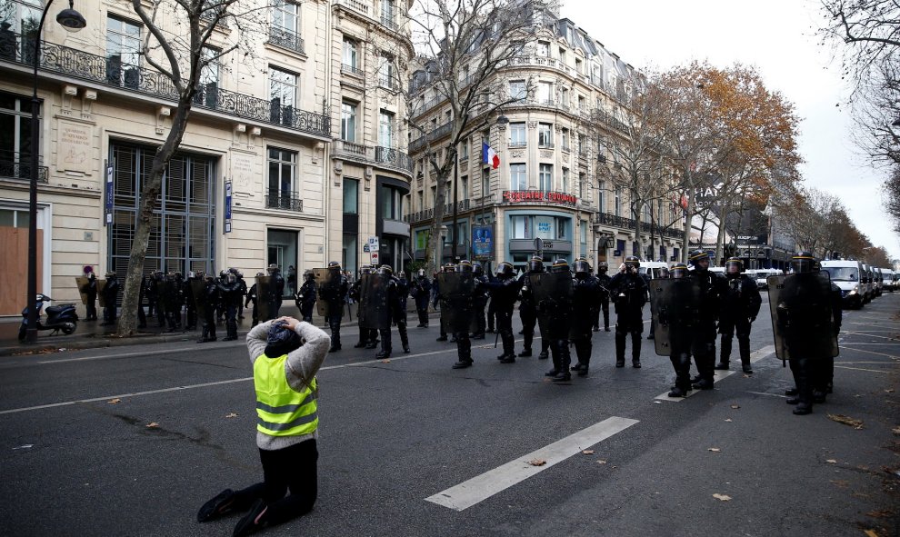 Un manifestante se arrodilla y posa sus manos sobre la cabeza mientras mira de frente a los policías antidisturbios que se protegen con sus escudos.- REUTERS/Stephane Mahe