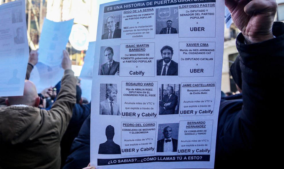 Un taxista ensaña un cartel en el que aparecen los nombres de varios cargos políticos y los trabajos -la mayor parte de ellos relacionados con VTC- que ocuparon cuando abandonaron la política. | Ricardo Rubio / Europa Press