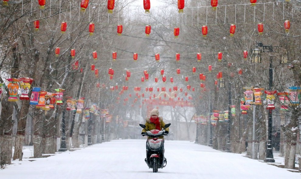 Una mujer conduce una motocicleta y pasa por una calle cubierta de nieve decorada con faroles, antes del Año Nuevo Lunar Chino, en Zhangye, Gansu | Reuters