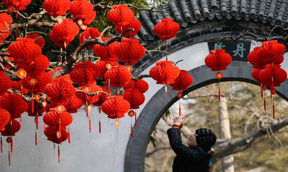 Una mujer usa su teléfono móvil para tomar una foto de las linternas rojas antes del Año Nuevo Lunar Chino en un parque en Beijing | AFP/ Wang Zao