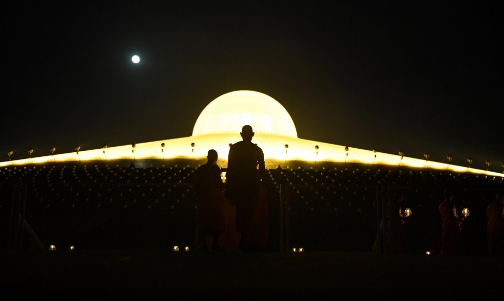 Monjes budistas que llevan velas encendidas mientras la luna llena se levanta durante las oraciones para conmemorar el Día de Makha Bucha en el templo de Wat Phra Dhammakaya, cerca de Bangkok | AFP/ Lillian Suwanrumpha